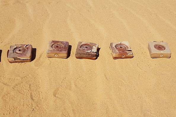 Quadratische Panzerminen liegen in einer Reihe auf Sand.