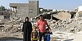 Ein Mann, eine Frau und zwei kleine Jungen stehen vor den Trümmern eines zerstörten Hauses.