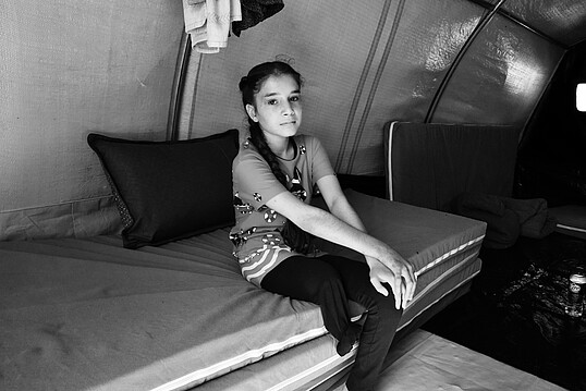 Shaded sitzt auf einem Bett und man sieht, dass ihr das rechte Bein fehlt. Dieses verlor sie auf der Flucht aus ihrer Heimat Mossul, aufgrund von Sprengsätzen die der Islamische Staat gelegt hat.