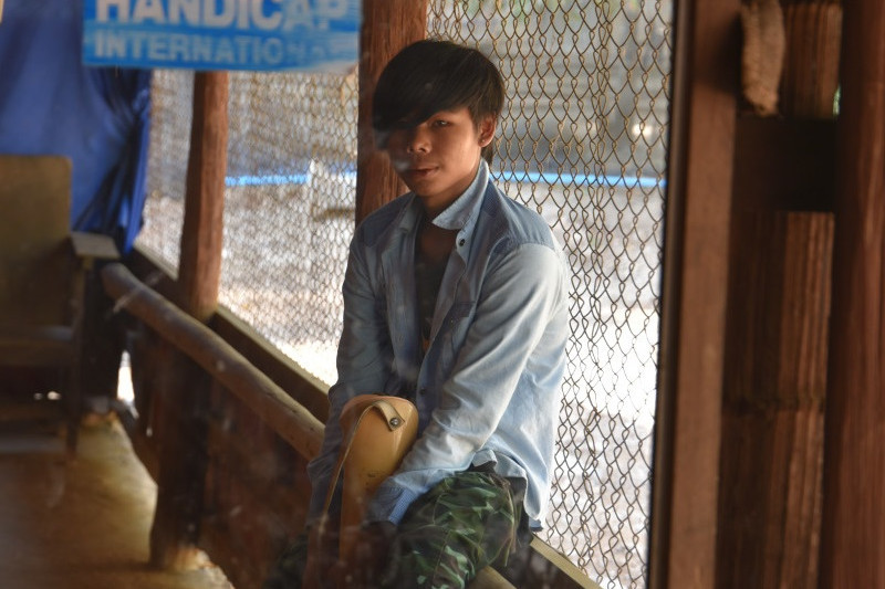Thailand Till Mayer Htee Soe Eh2 Htee steht vor dem Spiegel und hat seine Prothese in der Hand. Er hat immernoch einen ängstlichen Gesichtsausdruck.