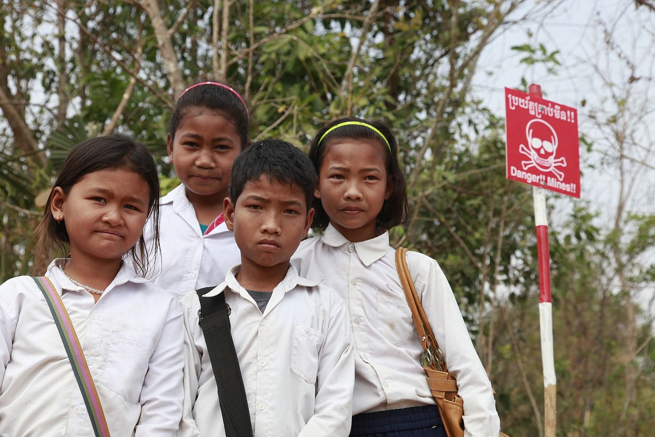 Vier Kinder stehen mit ernsten Gesichtern vor einem Danger Mines Schild