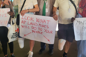 Zwei Minenopfer, die jeweils ein Bein verloren haben, stehen mit einem Schild, auf dem steht: "Seht, was Minen eurem Volk antun..." Auf dem Schild sind zwei Pfeile, die auf die fehlenden Beine zeigen.