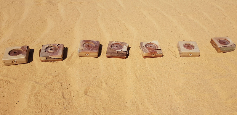 Quadratische Panzerminen liegen in einer Reihe auf Sand.