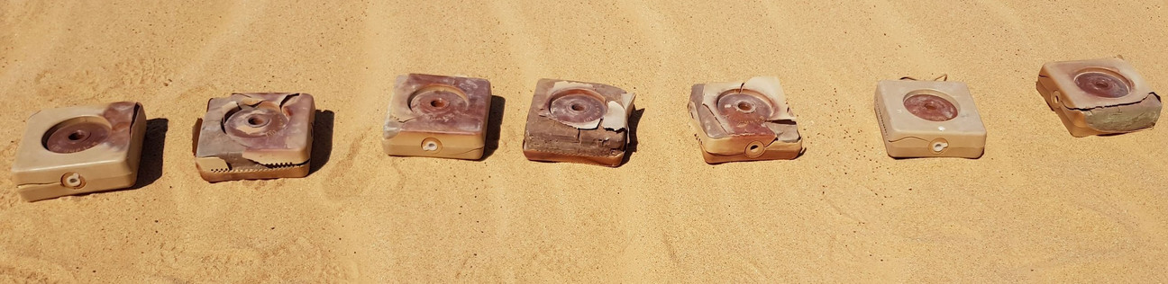 Quadratische Panzerminen liegen in einer Reihe auf Sand.