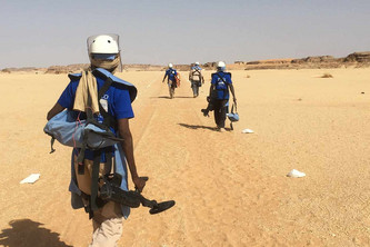 Ein Mann mit Entminungsausrüstung läuft anderen Männern hinterher.